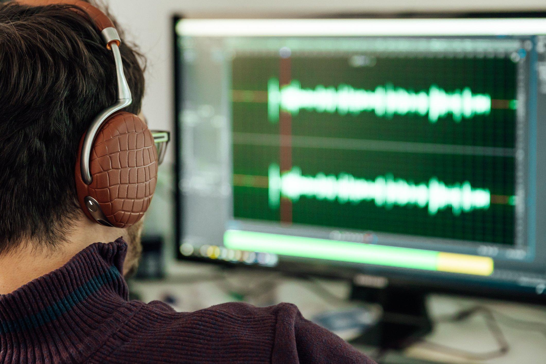 man at computer with headphones editing audio